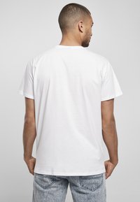 Hvid bomulds T-shirt med korte ærmer og rund halsudskæring, med en glat tekstur. Båret med slidte lyseblå denim jeans.