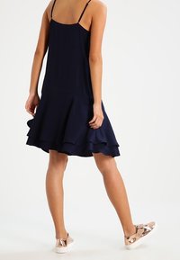 Mörkblå skjortklänning med spaghettiband, som har en utställd kjol och lager av fåll. Bärs med metallic rosaguld sneakers.