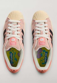 Różowe zamszowe trampki z czarnymi paskami, kremowym gumowym noskiem i białymi sznurowadłami. Na języku i wkładce znajdują się oznaczenia z postacią SpongeBob Kanciastoporty.