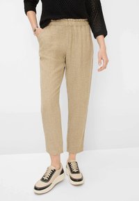 Pantalons en lin beiges avec une taille élastique, coupe fuselée et poches latérales, assortis à des baskets noires et crème avec un design à lacets.