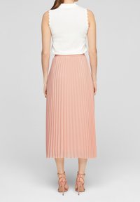 Top bianco senza maniche con bordi scallop abbinato a una gonna plissettata rosa fino al ginocchio. Include décolleté rosa con cinturini.