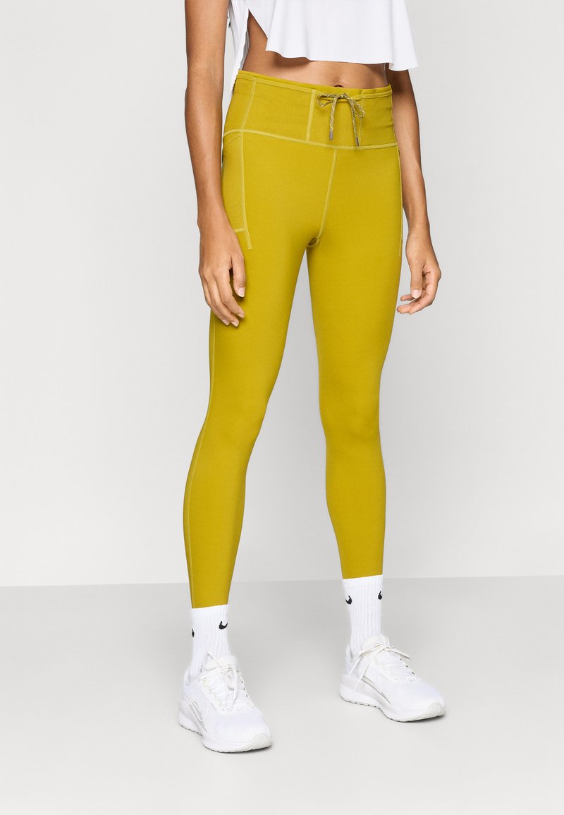 Κίτρινο αθλητικό κολάν με κορδόνι στη μέση, επίπεδες ραφές και πλαϊνές τσέπες. Συνδυάζεται με λευκά αθλητικά παπούτσια και κάλτσες με λογότυπο.