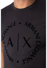 Svart bomull T-skjorte med et rundt grafisk logo som har teksten "Armani Exchange" og et "A/X" design i svart trykk på forsiden.