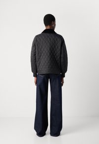 Quilted black jacket with a collar, long sleeves, and elastic cuffs, paired with wide-leg dark denim pants. Simple, functional design.