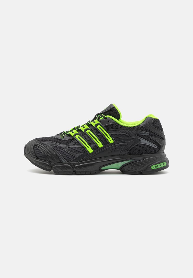 Black athletic shoe with green accents, featuring mesh upper, cushioned sole, and prominent stripes. Designed for comfort and support.