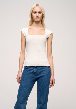 Top alb, ajustat, cu decolteu pătrat și mâneci scurte, fabricat dintr-un material texturat. Asortat cu blugi din denim albastru, cu croială lejeră.