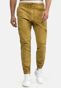 Khakifarbene Jogginghosen mit elastischen Bündchen und einem Kordelzugbund. Mit Cargo-Taschen und einem glatten, leichten Stoff.