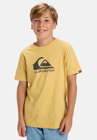 Žluté bavlněné tričko s černým logem Quiksilver a designem hory na přední straně. Krátké rukávy a volný střih.