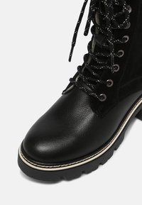 Stivale alla caviglia in pelle nera e suede con punta arrotondata, finitura testurizzata, cuciture bianche a contrasto e lacci a stampa bianca e nera.