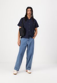 Navy short-sleeve button-up shirt, light blue wide-leg jeans, white sneakers with red accents, and a small black crossbody bag.