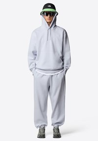 Ljusgrå hoodies med ficka fram och matchande sweatpants. Utstyrseln är kombinerad med grå och gula träningsskor och en svart hatt.
