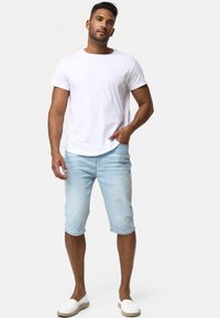 Camiseta blanca de manga corta, pantalones cortos de mezclilla azul claro que llegan a la mitad de la pantorrilla y espadrilles blancas. Conjunto casual con corte estándar.