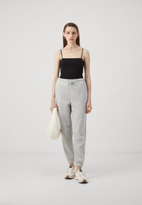 Svart cami-top, grå joggebukser med snøring og elastiske mansjetter, hvit veske og kremfargede sneakers med beige detaljer. Enkelt, casual antrekk.