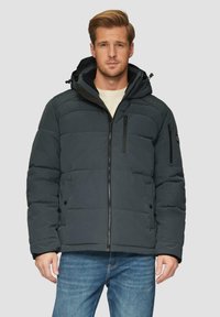 Ciemnoszara kurtka puchowa z zamkiem z przodu, regulowanym kapturem i zapinanymi na zamek kieszeniami na piersi; ma pikowaną teksturę. Noszona na jasnym swetrze.