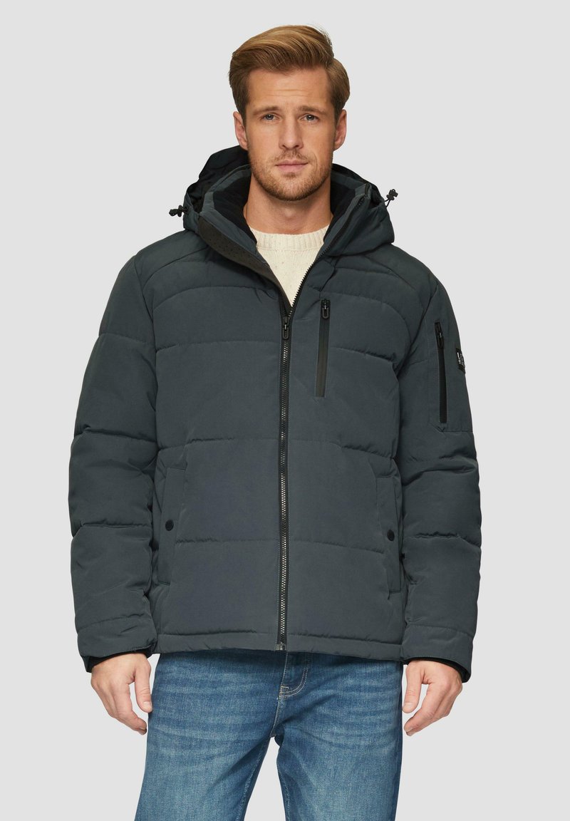 Ciemnoszara kurtka puchowa z zamkiem z przodu, regulowanym kapturem i zapinanymi na zamek kieszeniami na piersi; ma pikowaną teksturę. Noszona na jasnym swetrze.