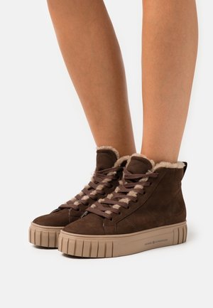 Zapatillas altas de ante marrón con cuello forrado de piel, suela de goma beige texturizada y cordones marrones con detalles claros.