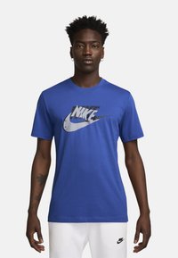 Camiseta Nike azul hecha de tejido suave, con un gran logotipo en blanco y negro en el frente. Manga corta y cuello redondo.