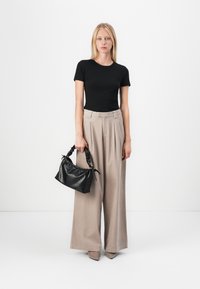 Sort tætsiddende kortærmet top, lys beige vidde bukser og en lille sort struktureret taske med et flettet håndtag.