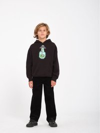 Sudadera negra con un estampado gráfico de un OVNI y un alienígena. Combinada con pantalones de pana negros y zapatillas negras. Fondo blanco liso.