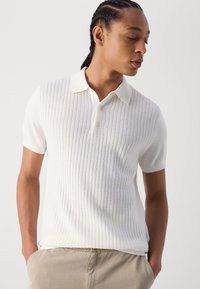Witte gebreide poloshirt met korte mouwen, met een textuur van ribbels. Zachte stof en een klassieke kraag. Geschikt voor casual uitstraling.