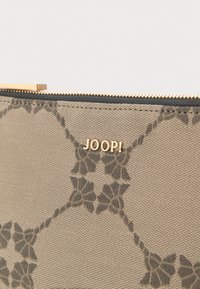 Beżowa saszetka z teksturowanej tkaniny, z ciemnym kwiatowym wzorem i złotym logo "JOOP!". Zamek błyskawiczny z akcentami w złotym kolorze.
