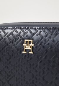 Borsa in ecopelle blu navy con un motivo geometrico in rilievo e un accento logo dorato. Texture liscia con cuciture ben definite.