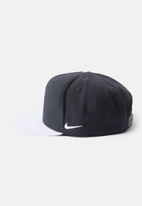 Granatowa czapka z białym daszkiem i logo Nike. Posiada strukturalny kształt, teksturę materiału oraz otwory wentylacyjne na górze.
