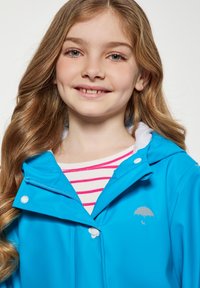 Ryškiai mėlyna, neperšlampama striukė su užtrauktuku ir sagomis, su balta pamušalu kapučiuku ir pilku skėčio logotipu ant krūtinės.