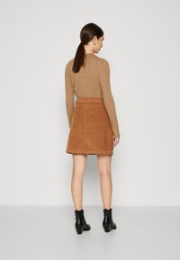 Bordeauxkleurige corduroy rok met een getailleerde taille en een uitlopende zoom, gecombineerd met een ribgebreide tan trui en zwarte enkellaarsjes.