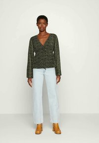Blusa de mangas longas, com decote em V profundo, na cor verde escuro, com estampa floral, combinada com jeans de perna reta azul claro e tamancos de salto na cor tan.
