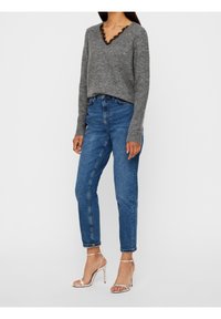 Grauer Strickpullover mit V-Ausschnitt und schwarzer Spitzenverzierung. Kombiniert mit hoch taillierter blauer Jeans und silbernen Riemchenabsätzen.