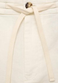 Pantalones cortos de lino color crema con cierre de cordón, un botón suave y un bolsillo delantero con detalles de costura.