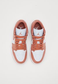 Paire de baskets Nike Air Jordan blanches et pêche avec lacets noués, vue du dessus sur un fond blanc uni.