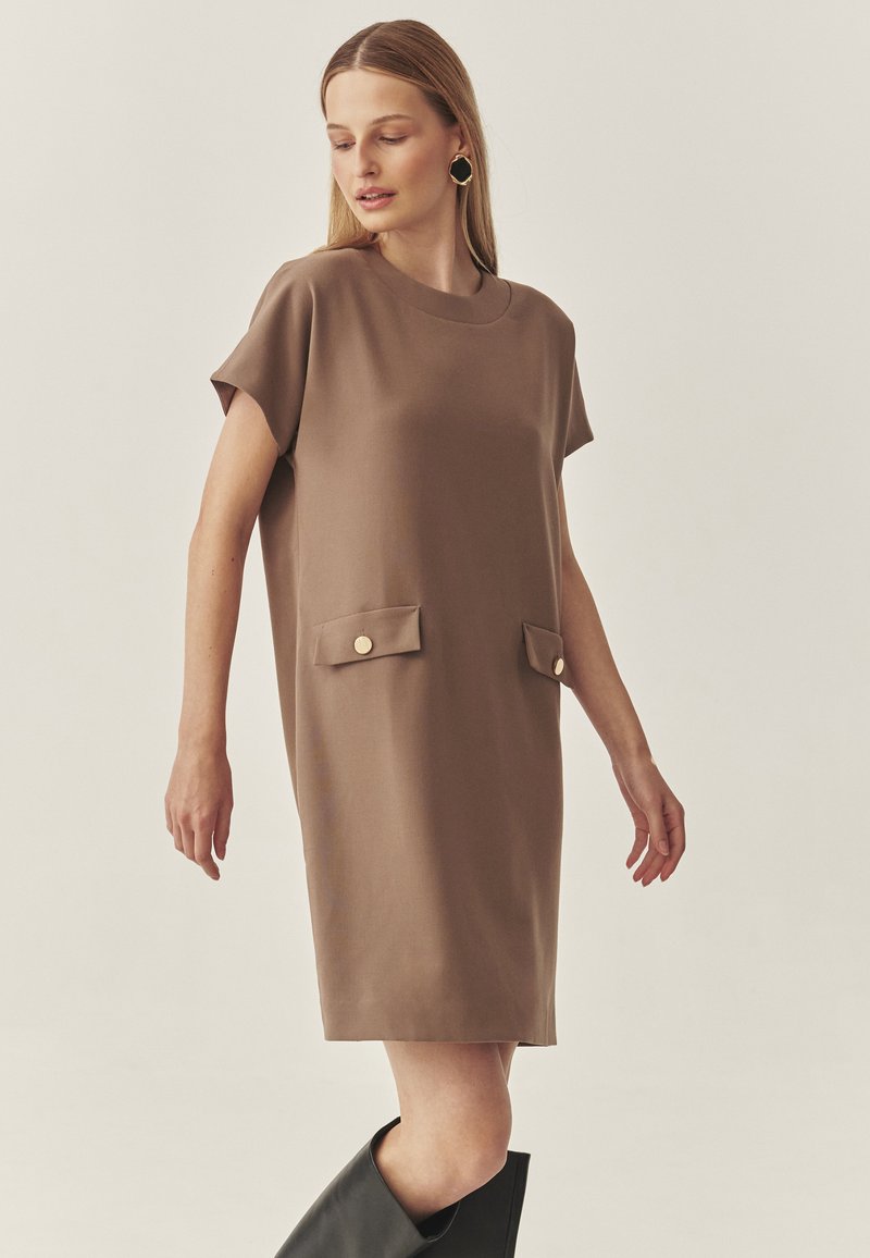 Braunes, kurzärmliges Kleid mit rundem Ausschnitt, zwei aufgenähten Taschen vorne mit goldenen Knöpfen und einer lockeren Silhouette.