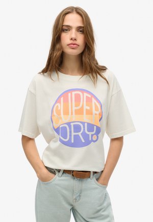 T-shirt à manches courtes de couleur crème clair, avec un grand logo circulaire multicolore "SUPER DRY" en orange, rose et violet. Coupe décontractée avec un col rond.