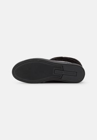 Zwarte rubberen zool met een gestructureerd grippatroon, ronde vorm en branding. Zacht zwart materiaal aan de bovenkant voor comfort en isolatie.