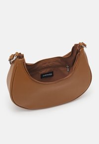 Sac d'épaule marron en forme de croissant avec fermeture éclair, bandoulière réglable et poche intérieure zippée montrant l'étiquette de la marque.