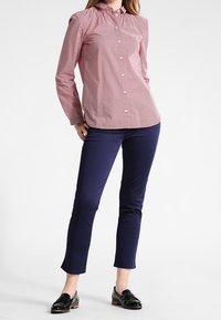 Punainen ja valkoinen pilkullinen napillinen paita, jossa kaulus, yhdistettynä tummansinisiin slim-fit-housuihin ja mustiin kenkiin. Silkkinen kangas, mittatilaustyönä tehty istuvuus.