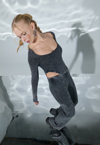 Grey, fitted bodysuit with long sleeves, scoop neckline, and side cutout. Worn with flared pants and black chunky boots.