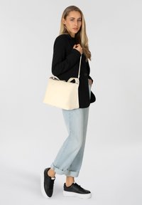 Sac en cuir crème au design structuré et aux poignées doubles, associé à un blazer noir, un jeans tapered bleu clair et des baskets noires.