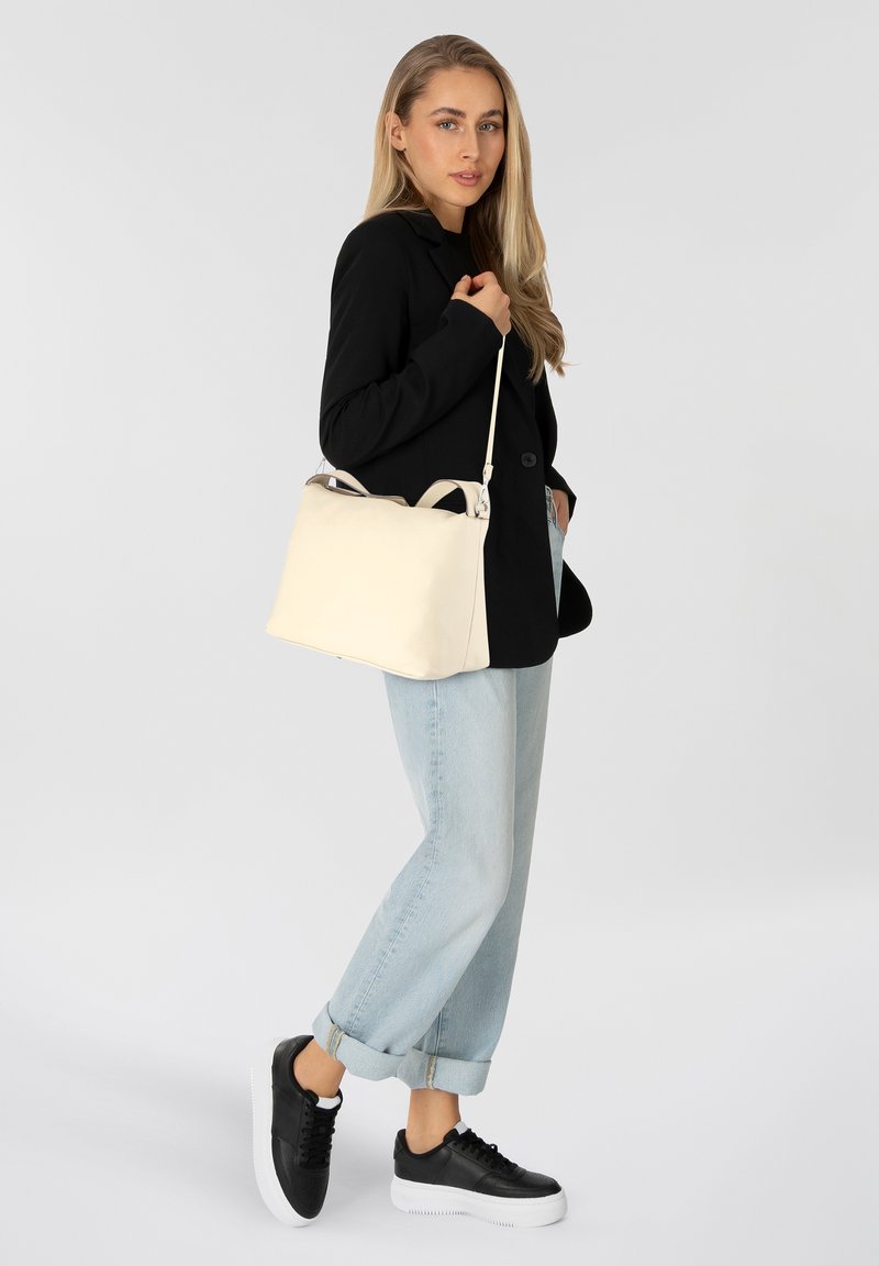 Sac en cuir crème au design structuré et aux poignées doubles, associé à un blazer noir, un jeans tapered bleu clair et des baskets noires.