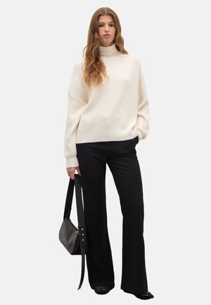 Suéter blanco de cuello alto acanalado con hombros caídos, combinado con pantalones negros de campana y un bolso negro con correa de hombro.