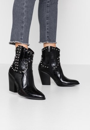 Czarne botki na kostkę z wzorem imitującym krokodylą skórę, zakończone szpiczastym noskiem, z srebrnymi ćwiekami po bokach i masywnym obcasem. Zamek błyskawiczny z tyłu.