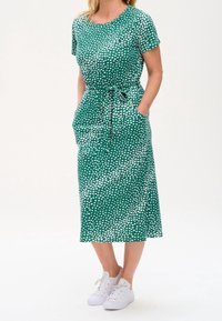 Green midi dress with white heart pattern, short sleeves, round neckline, drawstring waist, and side pockets, paired with white sneakers.