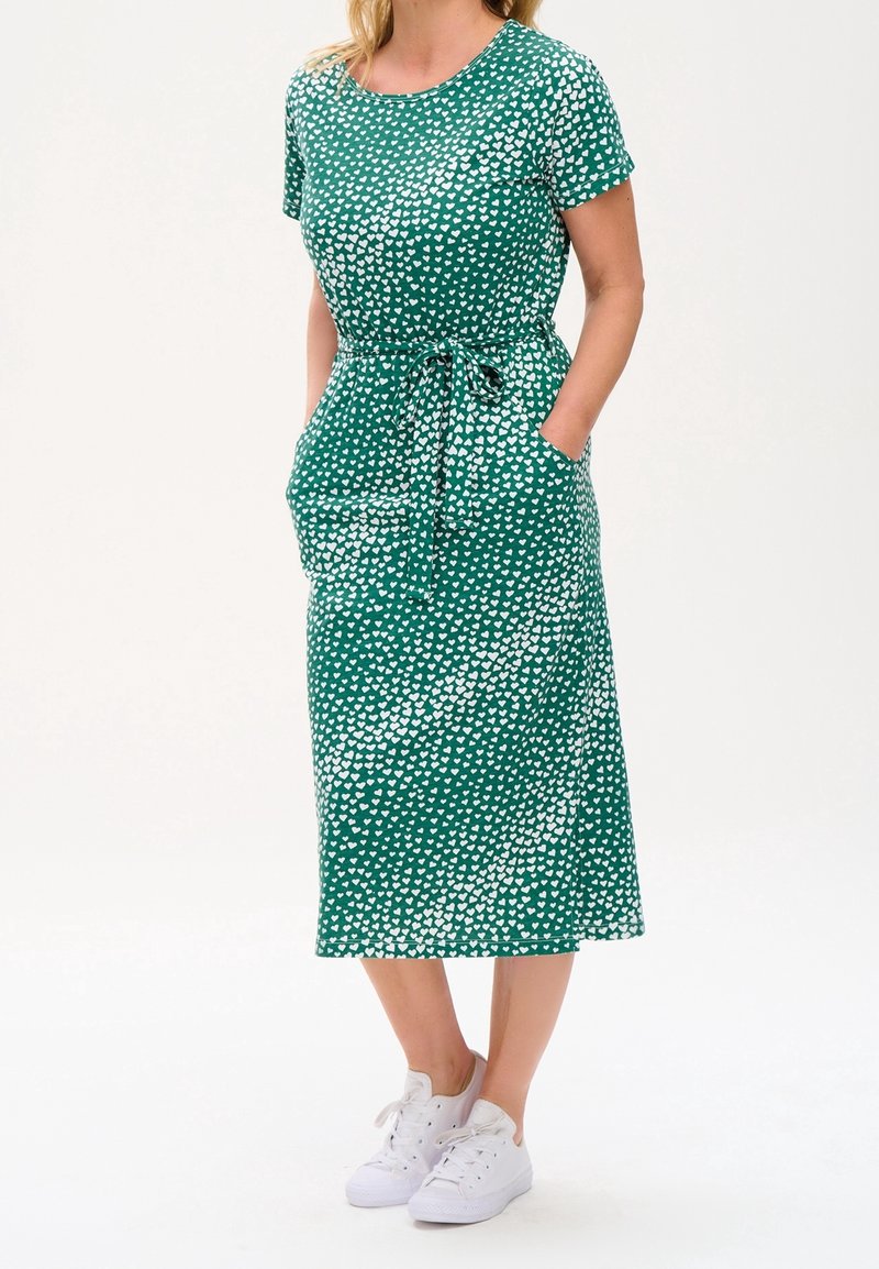 Green midi dress with white heart pattern, short sleeves, round neckline, drawstring waist, and side pockets, paired with white sneakers.
