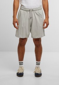 Pantaloni scurți atletici de culoare gri deschis, cu talie elastică, șnur și două buzunare laterale. Purtați cu un maiou alb simplu și adidași.
