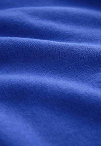 Close-up van zachte, gestructureerde blauwe stof met zachte plooien en subtiele schaduw die het gladde oppervlak van het materiaal benadrukken.