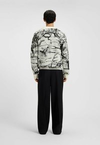 Sweater har et sort og hvidt træ- og uglemotiv på en lys baggrund, med elastiske manchetter og kant; parret med løse sorte bukser.