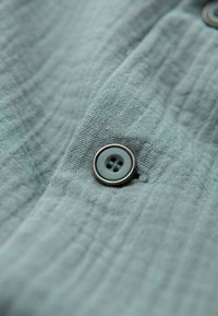 Tissu gris avec une texture de tissage visible avec un bouton rond à quatre trous cousu avec un fil assorti.
