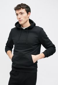 Zwarte hoodie gemaakt van zacht stof, voorzien van een capuchon met trekkoord, een zak aan de voorkant en geribbelde manchetten. Eenvoudig, minimalistisch ontwerp.